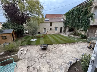 Une cour en pierre de pays des Yvelines, pelouse tondue en bandes, olivier et terrasse en dallage